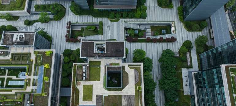 Vue aérienne d’un quartier dense intégrant des toits verts, des arbres et des espaces végétalisés, illustrant comment le verdissement urbain peut atténuer les îlots de chaleur en milieu bâti.